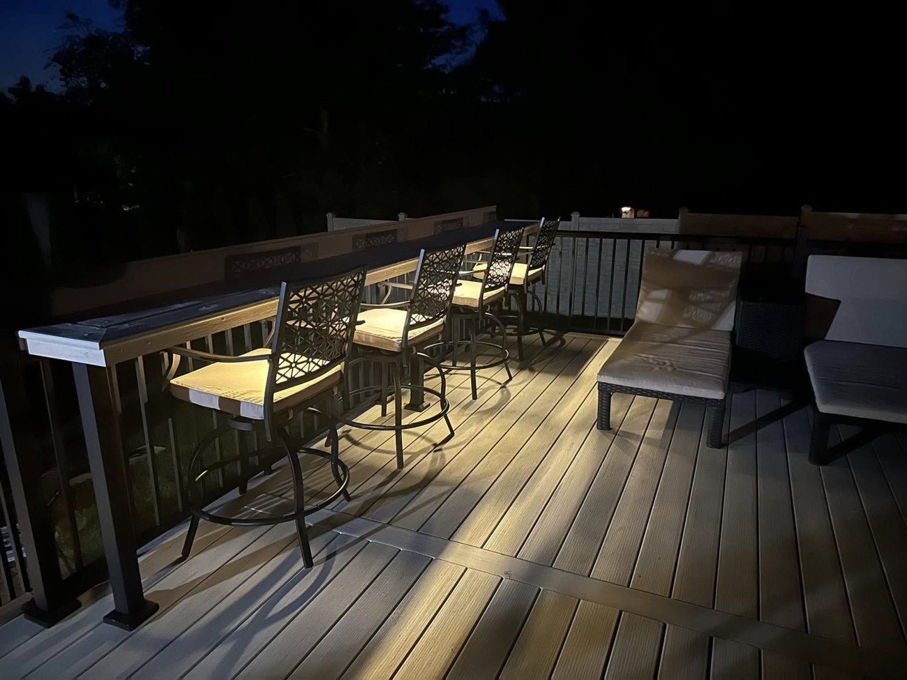 Composite deck with a custom bar rail and step lighting, built by Layer Carpentry